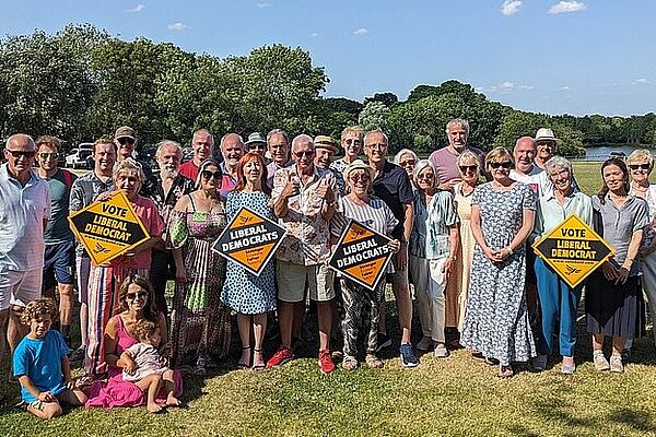 A crowd of varied Liberal Democrats in a country park including some holding Liberal Democrat diamond posters