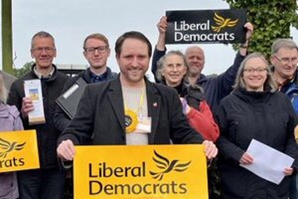 A group of enthusiastic Liberal Democrats displaying gold posters and campaign leaflets
