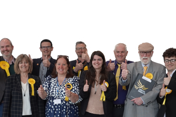 A group of Liberal Democrats wearing yellow rosettes and celebrating with cheering and thumbs up