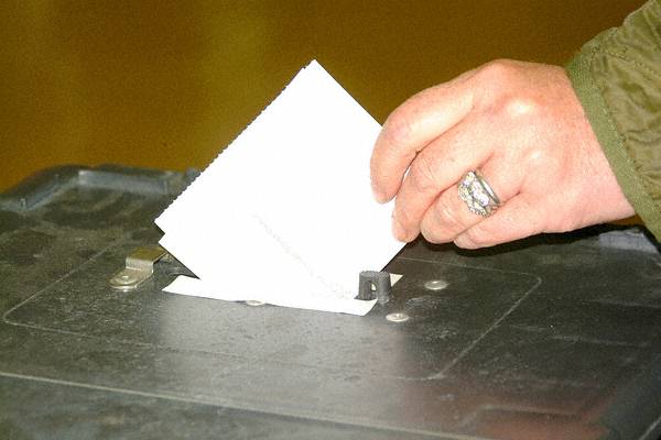 Voter's hand inserting ballot paper into black ballot box